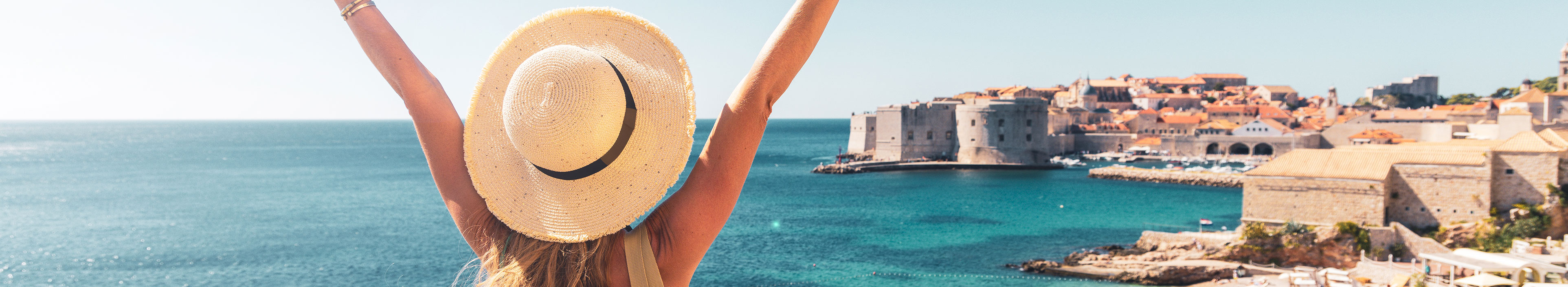 Frau streckt Arme in die Luft an der Küste in Dubrovnik, Kroatien