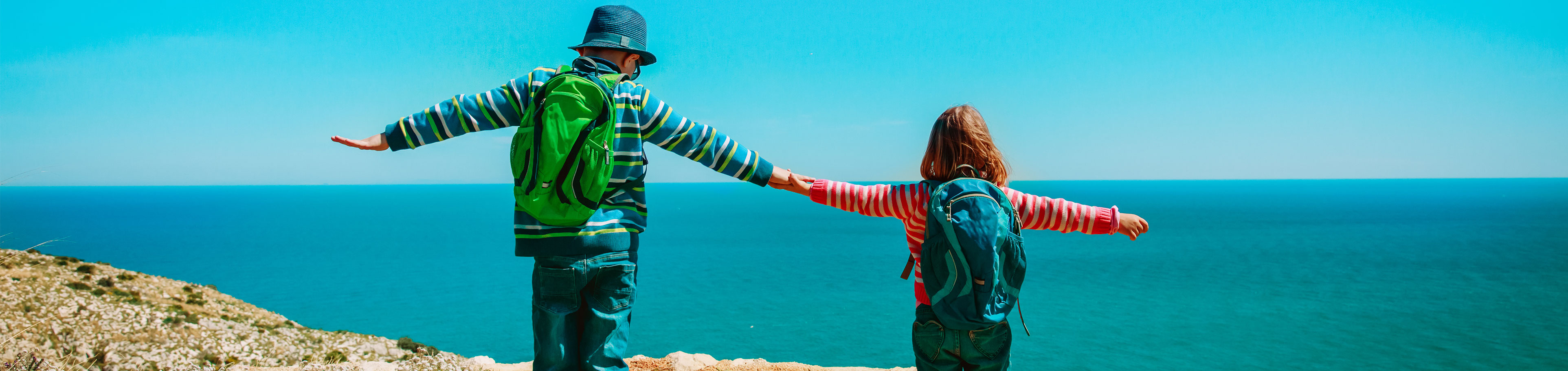 Zwei Kinder mit Rucksäcken mit dem Blick aufs Meer.