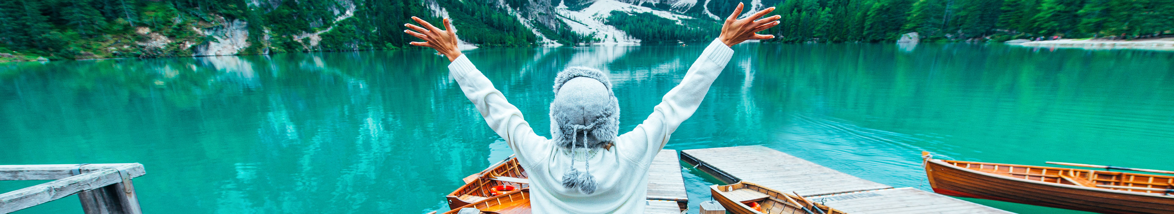 Eine fröhliche Frau blickt auf einen türkisblauen See und schneebdeckten Bergen