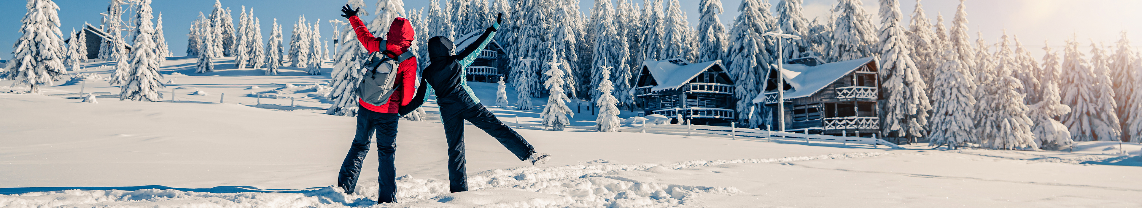 Paar in Skianzügen mit Rucksack blickt auf schöne Aussicht mit schneebedeckten Tannen in gefrorener Berglandschaft. Reisehintergrund. Alpines Skigebiet, Winterurlaub mit Lidl Reisen