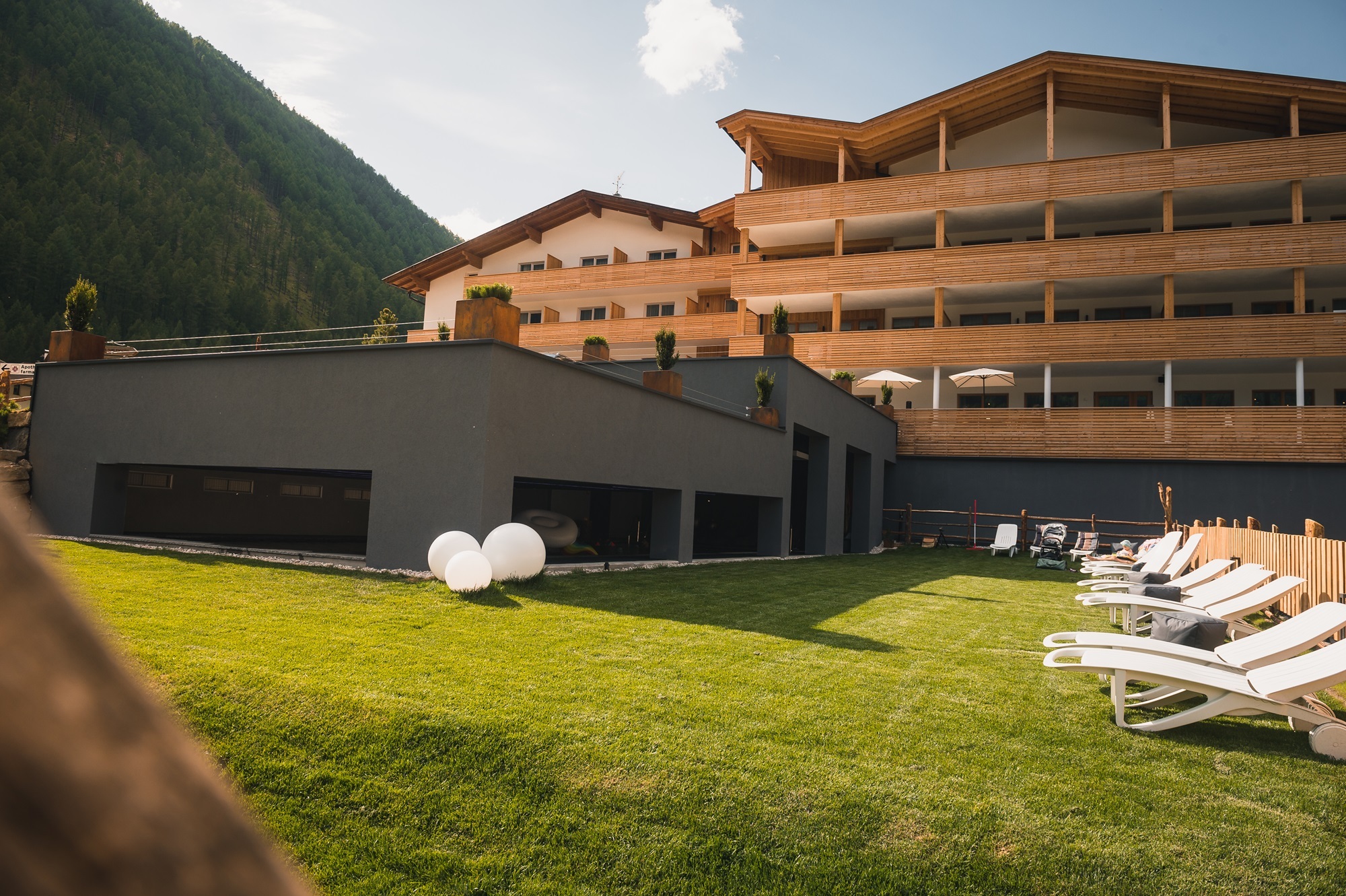 Außenbereich des Wellnesshotels Adlernest mit Liegewiese, Sonnenliegen vor bergbewachsenem Hintergrund.