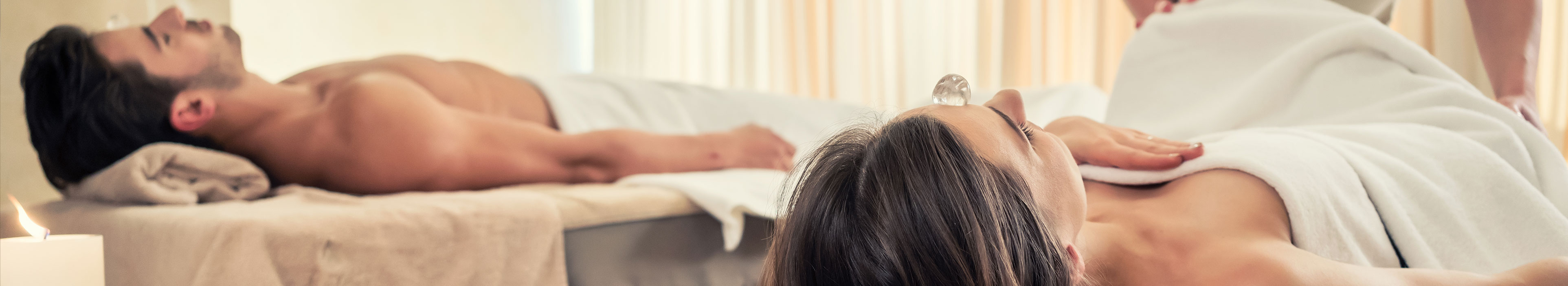 Junges Paar, das während einer Kristalltherapie in einem asiatischen Spa- und Wellnesszentrum auf Massagebetten liegt