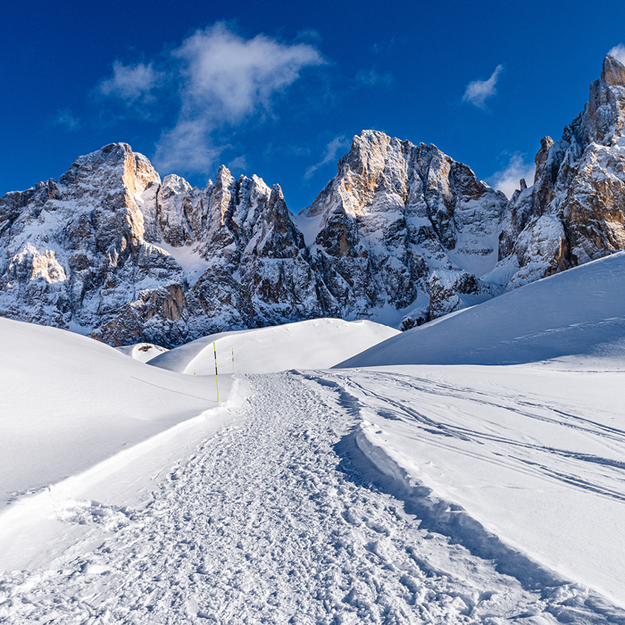 Winterwanderweg in einer tief verschneiten Landschaft vor markanten Felsgipfeln.