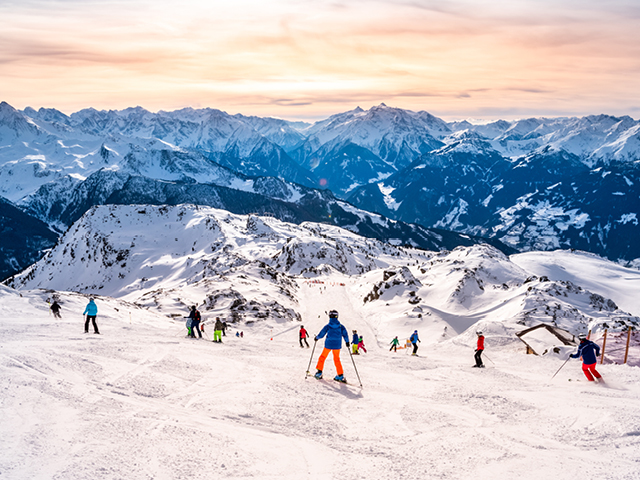 Skifahrer auf einer verschneiten Skipiste im Hochgebirge bei Abenddämmerung.