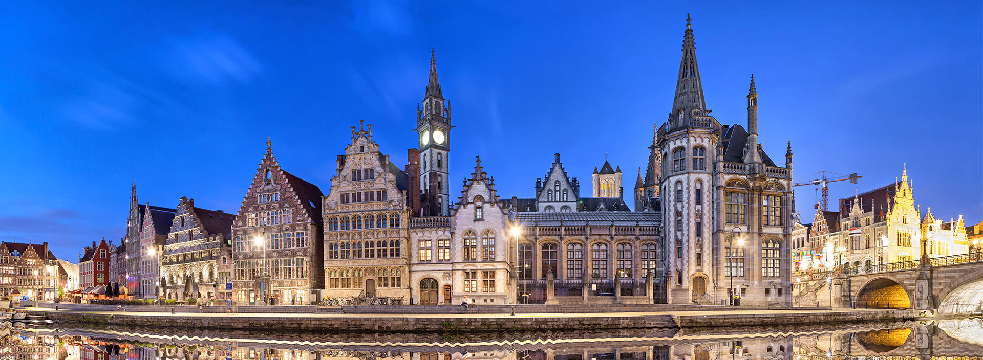 Die Skyline der Stadt Gent in Belgien spiegelt sich bei Nacht in einem Fluss.