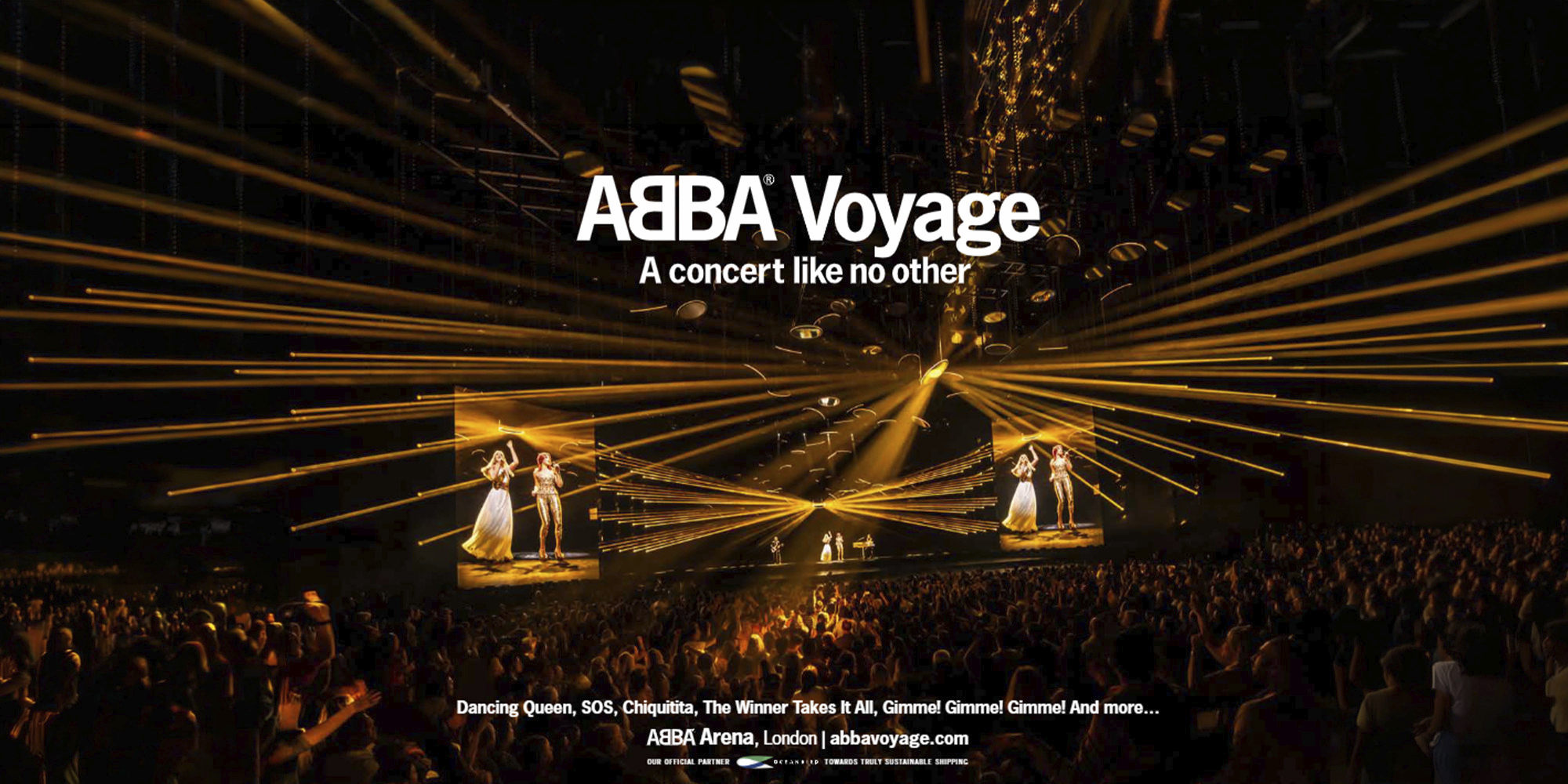 Blick im Panoramaformat in die vollbesetzte ABBA Arena in London während der virtuellen „ABBA Voyage“ Show. Unzählige goldene Laserstrahlen durchschneiden den abgedunkelten Raum über den Köpfen des Publikums. Auf großen Bildschirmen im Hintergrund sind die digitalen Avatare der Bandmitglieder zu sehen. Der Schriftzug „ABBA Voyage – A concert like no other“, bekannte Songtitel und die Webadresse sind als Text im Bild integriert.