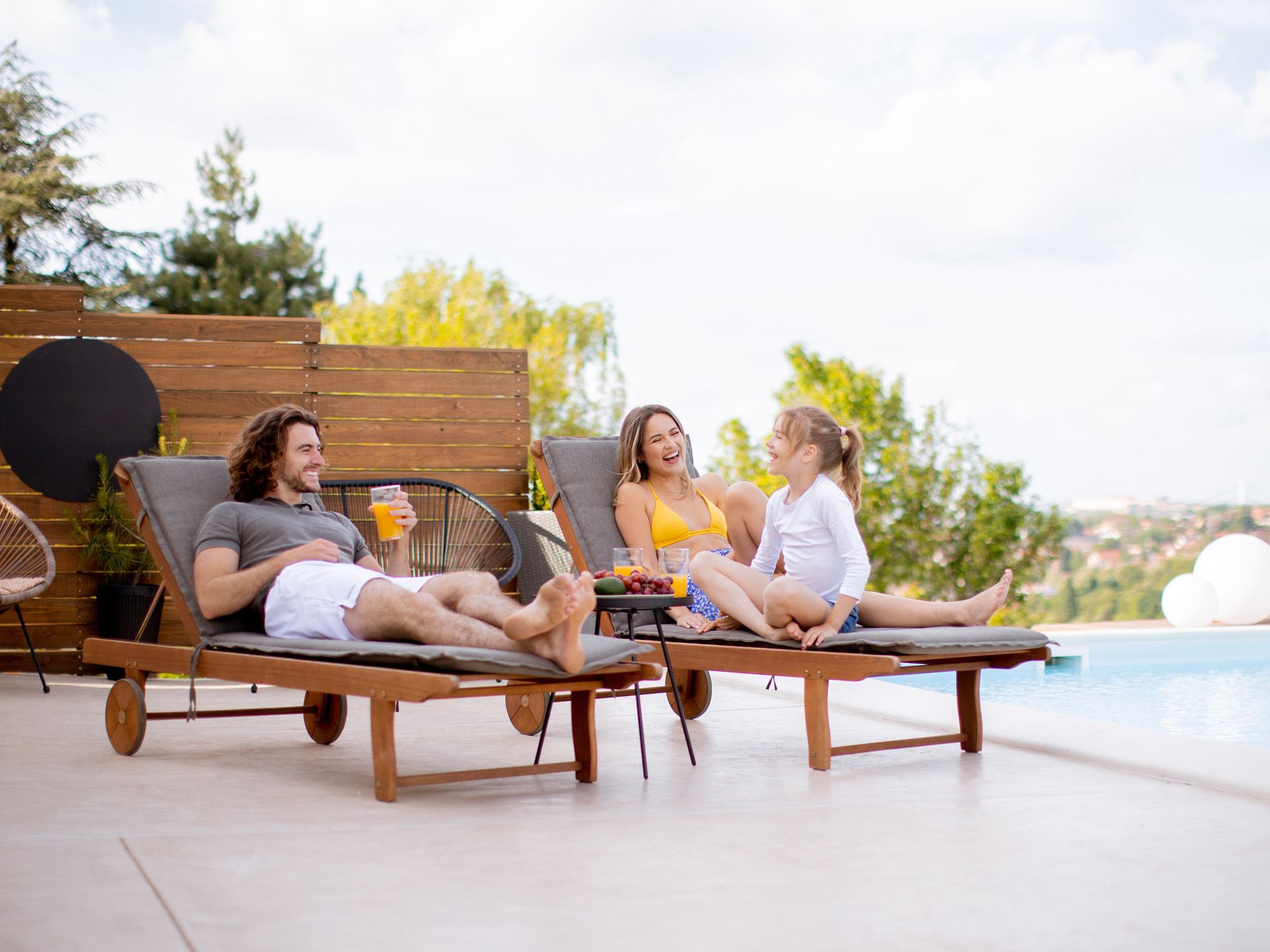 Eine Familie entspannt auf den Sonnenliegen am Pool ihres Ferienhauses.