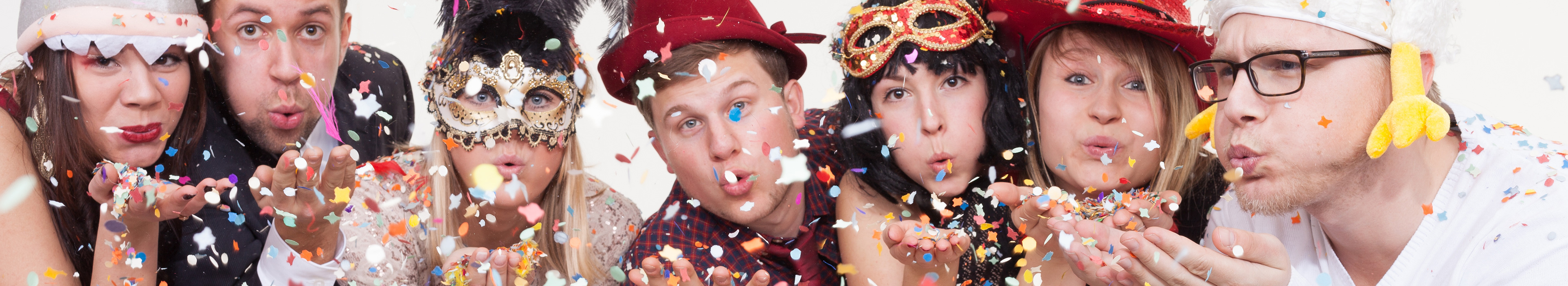 Eine gruppe Erwachsene in Faschingskostüme blasen Konfetti in die Luft und genießen ihre freie Zeit in den Faschingsferien.