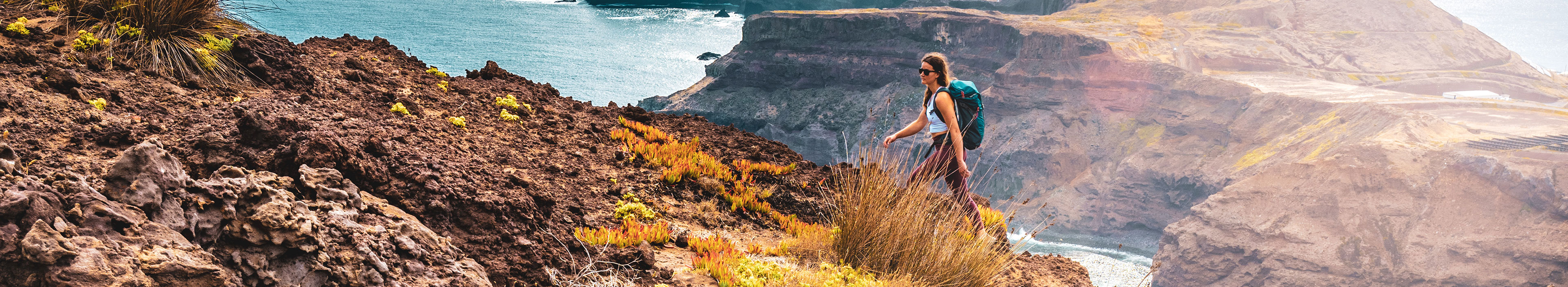 Eine Rucksacktouristin genießt die morgendliche Wanderung entlang einer steilen Klippe mit Blick auf das Meer und die zerklüfteten Ausläufer der Küste Madeiras.