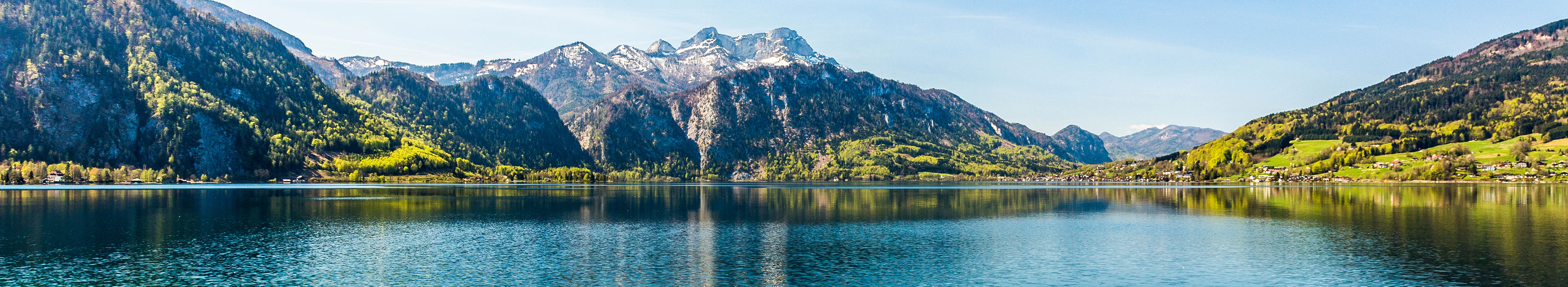 See in Österreich, Berge im Hintergrund, türkisblaues Wasser im Vordergrund.