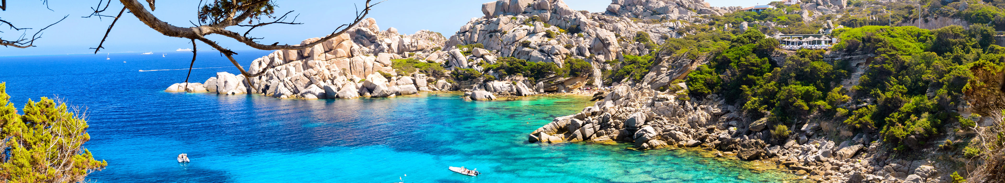 Urlaub Sardinien. Felsenbucht mit türkisblauem Wasser und weißen Fischerbooten.