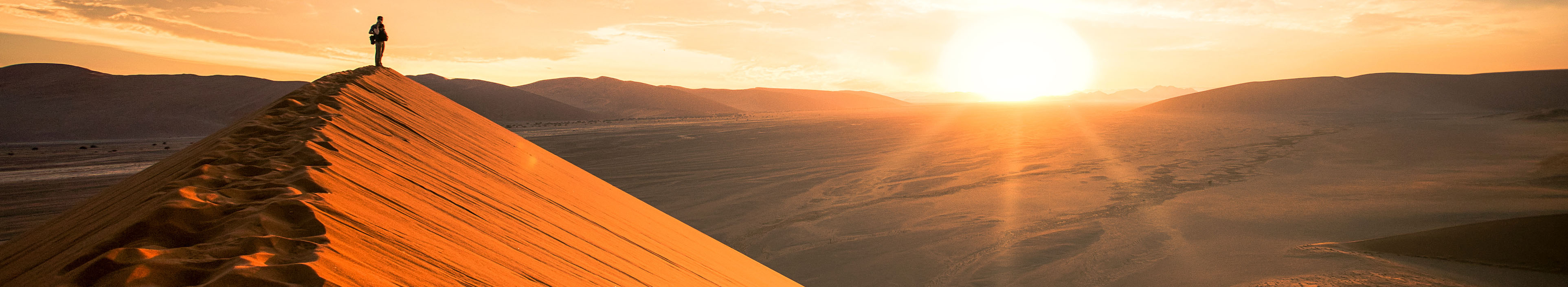 Ein Tourist steht auf einer großen Düne, bei Sonnenaufgang in Namibia.
