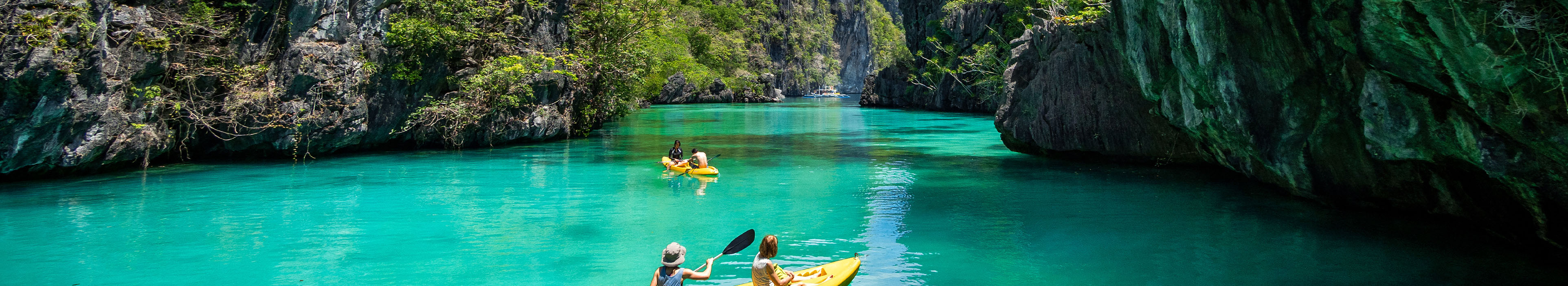 Touristen fahren Kajak in türkisblauem Wasser, umgeben von Felsen, Philippinen