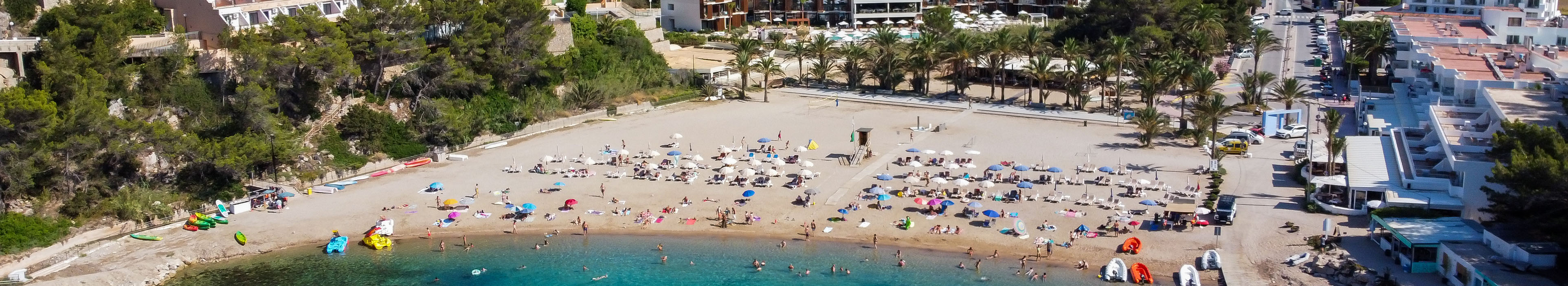 Strand auf Ibiza, im Hintergrund sieht man Hotels, im Vordergrund blaues Meer und Sonnenschirme