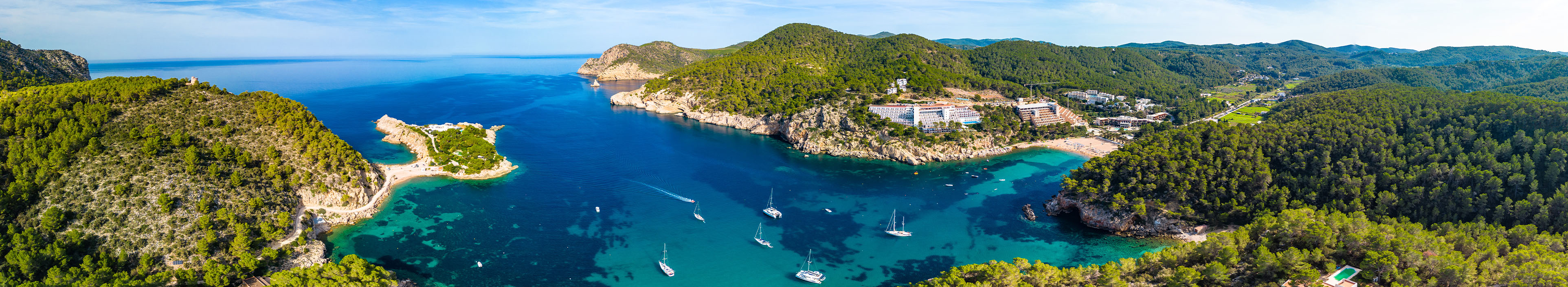 Bucht auf Ibiza mit türkisem Meer, Booten, Wäldern.