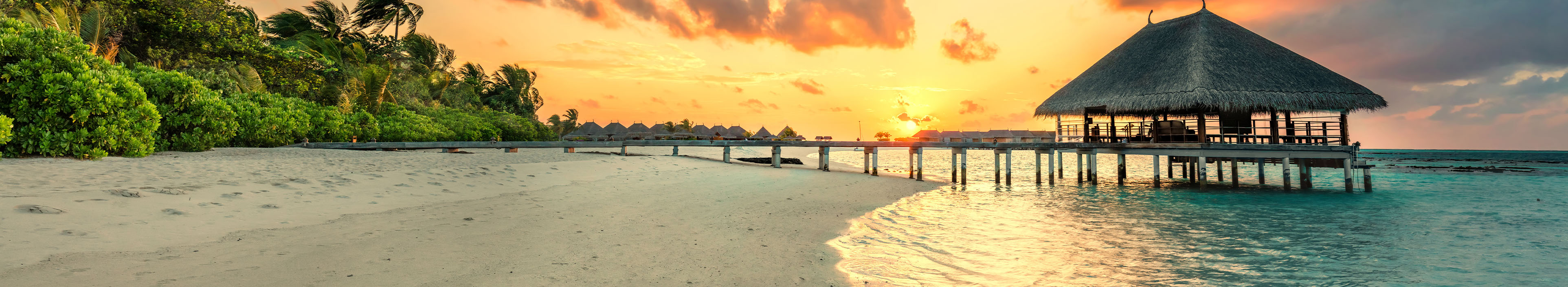 Strand mit Steg auf den Malediven bei Sonnenuntergang
