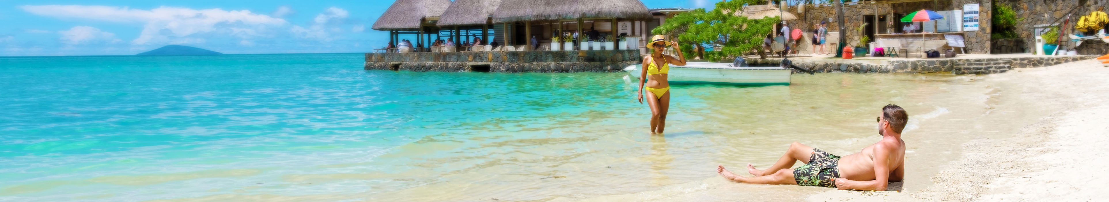 Paar am Strand und im Meer auf Mauritius, im Hintergrund Palmen und Hütten