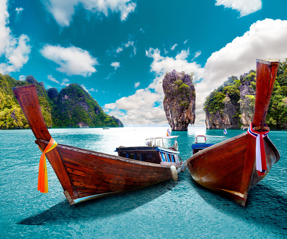 Urlaub Thailand. Zwei rote Holzboote auf türkisblauem Wasser und im Hintergrund Felsen.