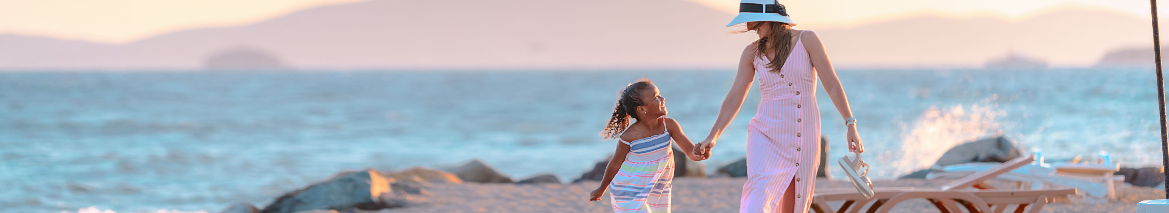 Frau und Kind laufen Hand in Hand am Strand zwischen Liegen und Sonnenschirmen auf Zypern