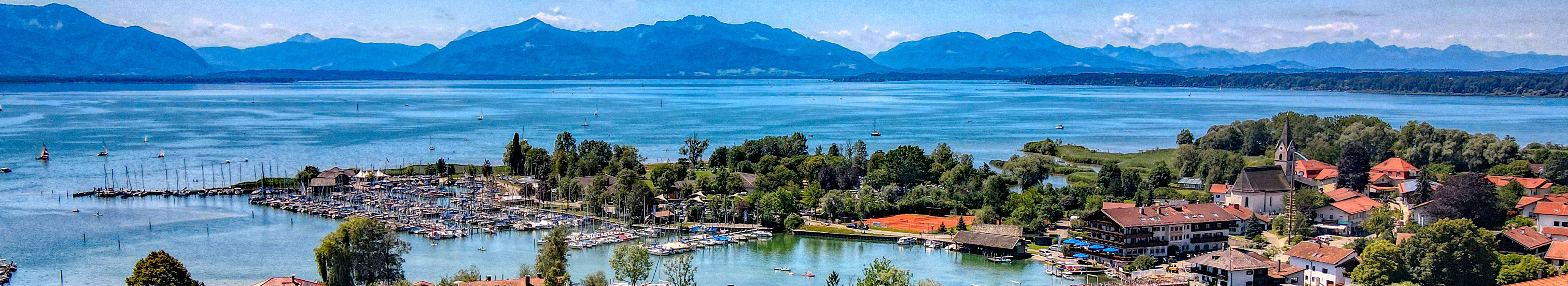 Blick auf den Chiemsee, eine Stadt im Vordergrund, im Hintergrund Berge.