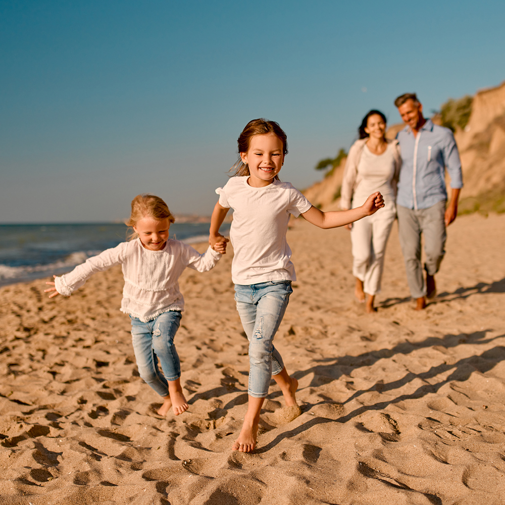 zwei kleine Mädchen rennen Hand in Hand freudig über einen breiten Sandstrand...